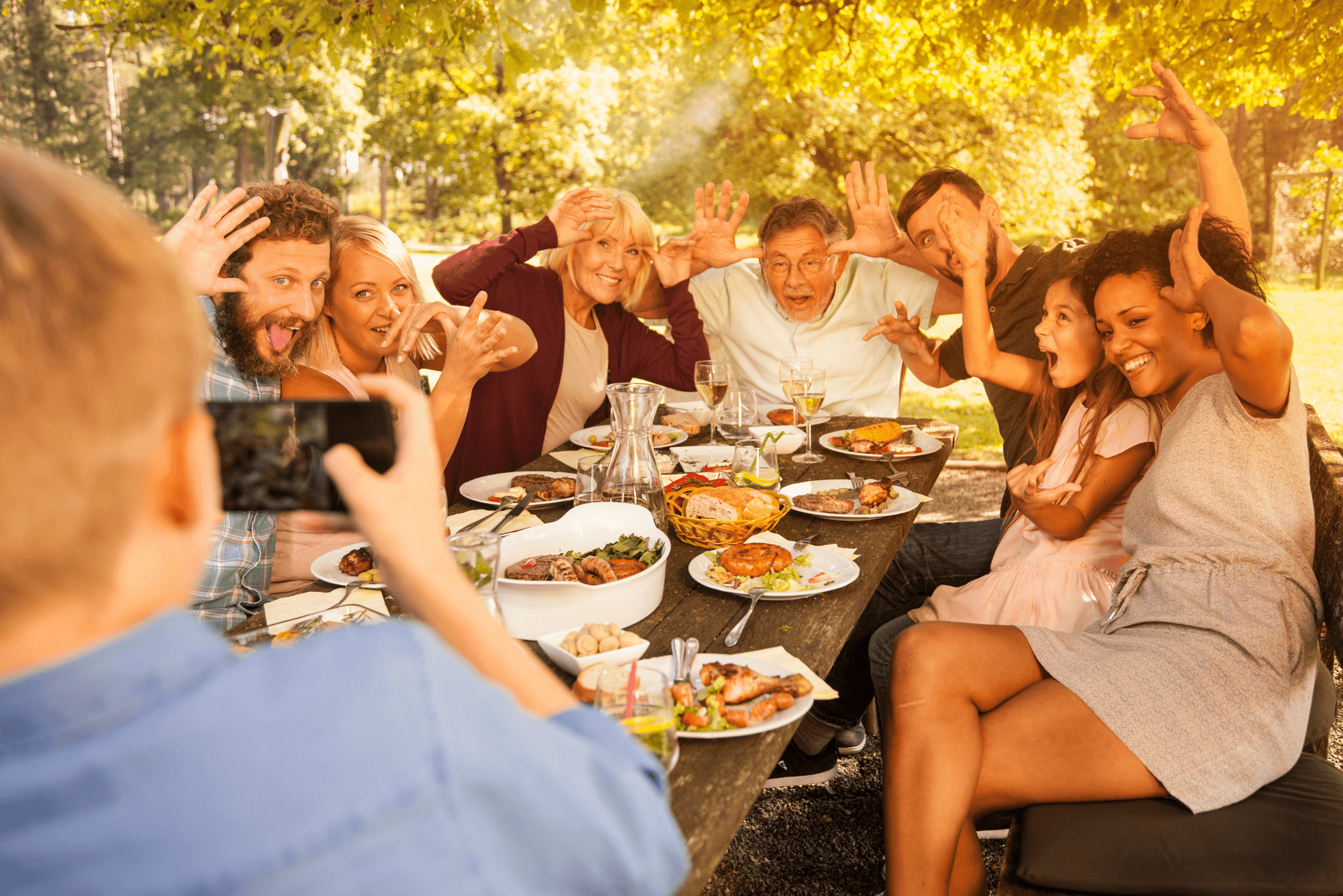 Familia diversa haciendo muecas divertidas para una foto durante una comida soleada al aire libre.